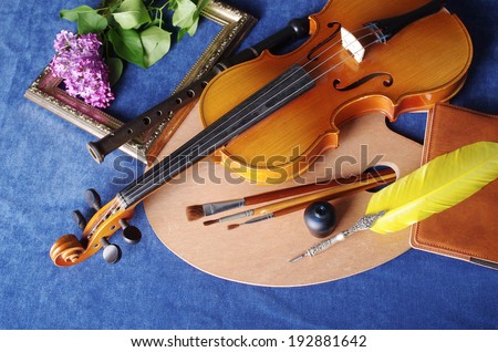Still life with violin, art palette, brushes, pen, bunch of lilac on the blue table-cloth
