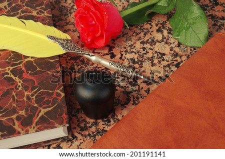 Old book, rose, feather pen and inkwell on granite table
