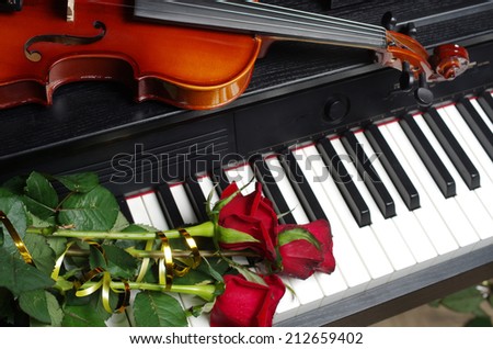 Three red roses and violin on a piano keyboard