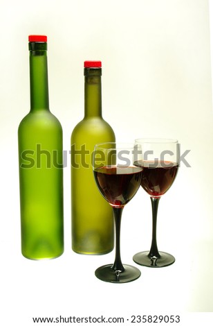 Two glasses of red wine and two green  bottles on white.