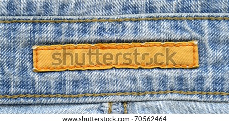 Blank yellow textile label  sewed on a blue jeans. Can be used as background for your text.