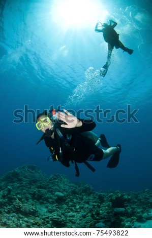 happy couple scuba diving together in clear blue ocean with coral reef behind in the red sea