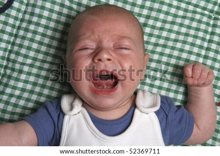 Crying eight week old newborn baby boy on a green play mat