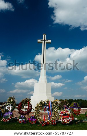 Marble Cross at war memorial with flowers under blue sky