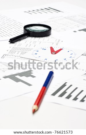 Financial charts and graphs on the table with magnifying glass, colored pencil and paper clock. Focus on the paper clock.