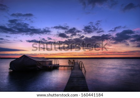 A beautiful autumn sunrise on the shores of Lake Cayuga in the Finger lakes region of New York state. A pier leads out to a deck with chairs for watching the fabulous sunrise.