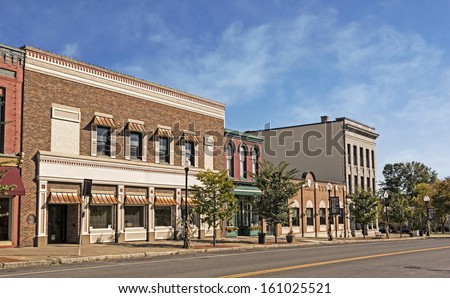 A photo of a typical small town main street in the United States of America. Features old brick buildings with specialty retail shops and restaurants. Decorated with autumn decor.