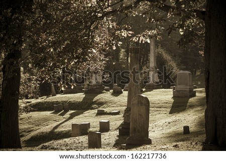 Photo of an old cemetery showing several elegant grave stone markers on a rolling hill.  Processed to look like a vintage  photo with washed out colors.