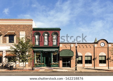 A photo of a typical small town main street in the United States of America. Features old brick buildings with specialty shops and restaurants. Decorated with autumn decor.