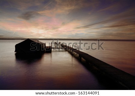 A beautiful autumn sunrise on the shores of Lake Cayuga in the Finger lakes region of New York state. A pier leads out to a power boat shelter and a deck with chairs for watching the sunrise.