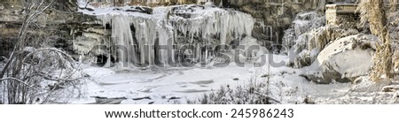 Panoramic photo of West Elyria Falls Ohio during winter. This cascading waterfall is in Elyria Ohio. The viewing platform on the right shown covered in ice along with the tree next to it.