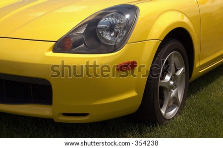 Front end of a yellow sports car parked on grass.