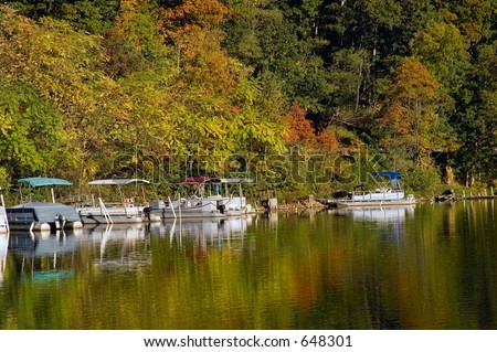 Pontoon boats docked on a lake. Fall colors reflecting n the calm waters.