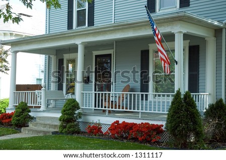 A typical front porch of a home in a small town in  the U.S.A. Featuring an American flag proudly flying and a porch swing to enjoy the spring day.