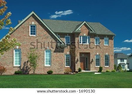 Large brick home with a lush green lawn and a beautiful blue sky background.