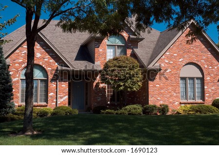 Beautiful red brick home featuring arched windows and beautiful mature trees.