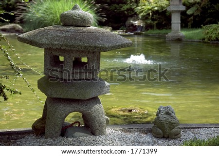 Beautiful weather worn stone pagoda and frog sitting next to a Japanese water garden. Shallow depth of field with Pagoda and frog in focus, blurred waterfall in background.