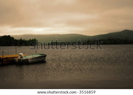 Dusk setting in on a lake with storm clouds overhead. Framed with a fishing boat in the foreground anchored to a pier. This beautiful lake is one of many located in New York\'s Adirondack mountains.