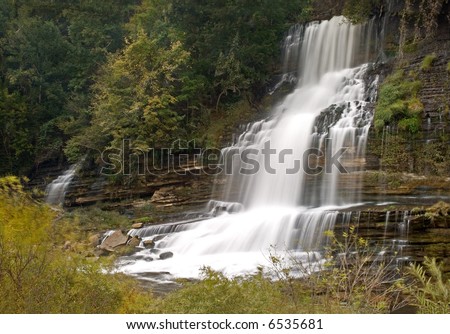 Beautiful cascading waterfall along a river in Tennessee. A touch of autumn colors in the trees and bushes.