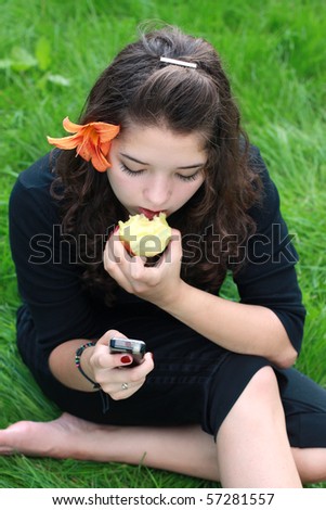 girl-teenager about a cellular telephone also eats an apple, on a grass.