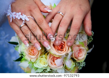 Hands of a newly-married couple, wedding rings and flowers.