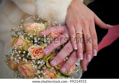 Hands of a newly-married couple, wedding rings and flowers.