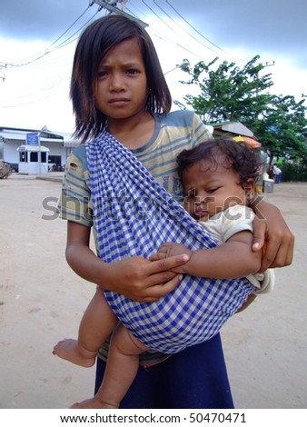 CAMBODIA BORDER, THAILAND - OCTOBER 07 : Young Cambodian girl carries her sister begs for money on the Thai Cambodian border October 07, 2007 in Cambodia border, Thailand.