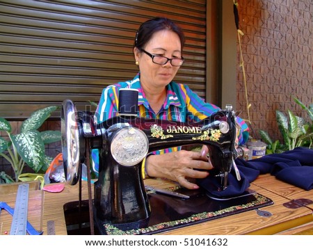 BANGKOK, THAILAND - APRIL 03: Thai woman sits by the roadside making clothes with a sewing machine in Bangkok. April 03 2007 in Bangkok.