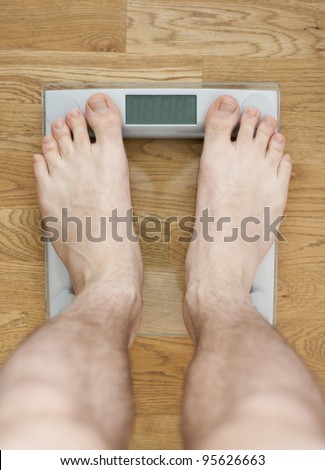 Young barelegged male standing on a transparent digital glass scale on a wooden floor. Room for your text in the display.
