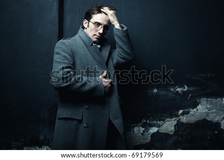 Artistic dark portrait of the young beautiful man in a gray coat against the destroyed wall