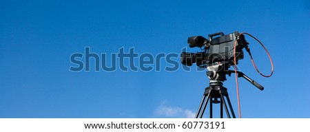 Professional digital video camera on tripod, on blue sky background