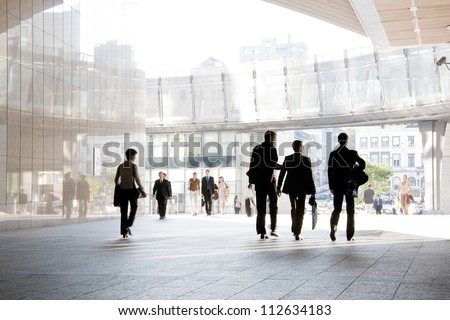 A Group Of People Is Against The Backdrop Of Modern Buildings. Blurred Motion. Silhouette.