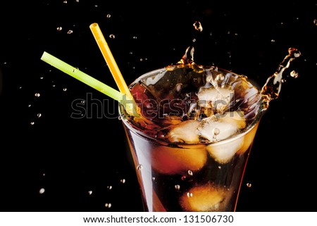fresh cola juice and ice cubes splash in a glass on black background