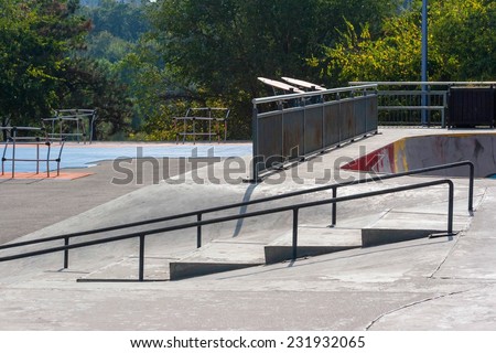 Empty skatepark at noon with ramps, grind rails, half pipe and fitness equipment.