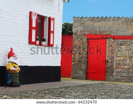 Garden gnome guarding picturesque farmhouse and barn bright with bright red painted doors