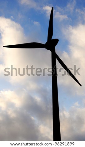 Silhouette of wind turbine or windmill against blue sky with white clouds