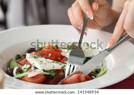 Picture of woman\'s hands with fork, knife and greek salad