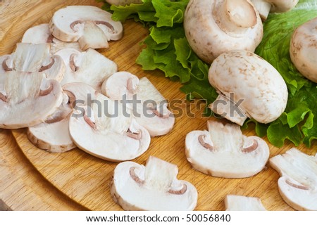 Closeup of champignons and green salad leaves on wooden cutting board