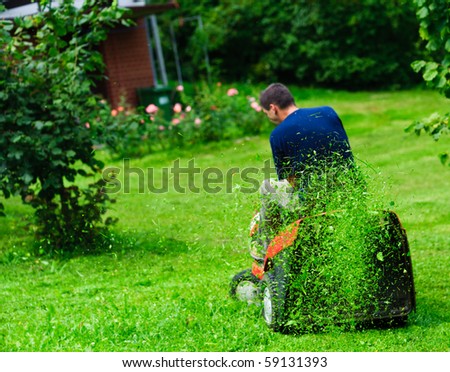 Ride-on lawn mower cutting grass. Focus on grasses in the air