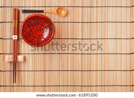 Chopsticks, spoon and red bowl on bamboo background with copyspace. Japanese still-life.