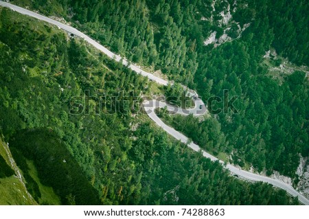 Mountain road aerial view. Asphalt zigzag in green forest.