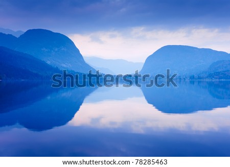Blue mountains reflected in lake water. Bohinj lake, Slovenia.