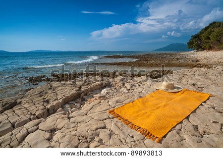 Wild Adriatic sea beach with rug for sun tanning. Croatia, Losinj island, popular touristic destination.
