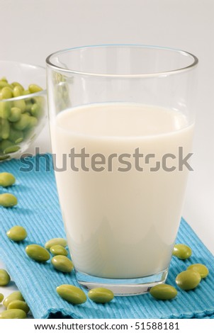 Soy milk in a glass. Fresh soy beans in foreground. White background.