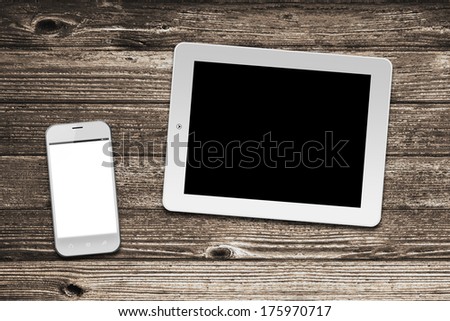 White tablet computer and smart phone with isolated screens on old wooden desk.