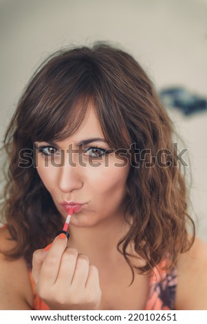 Attractive young woman with tousled brunette hair applying her lipstick and looking flirty in a fashion and beauty concept