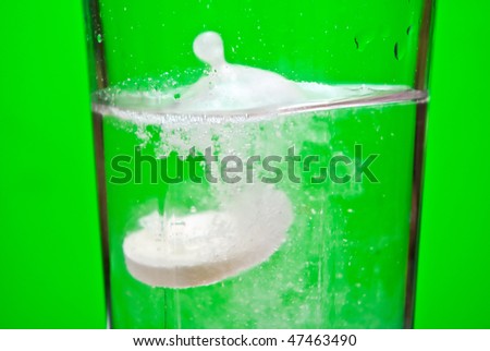 Effervescent tablet dissolving in water on green background