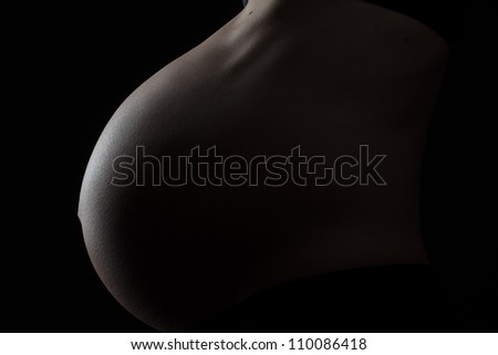 A pregnant woman\'s belly at 35 weeks. (Photographed with low key side lighting technique to create a rim of light defining the shape of the belly)