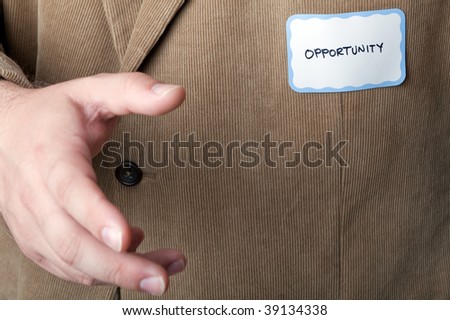 Man in a corduroy sport jacket reaching for a handshake and wearing a name tag that says \
