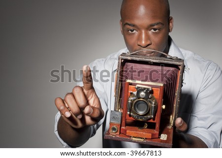 African American photographer gesturing and holding an old-fashioned large format camera.